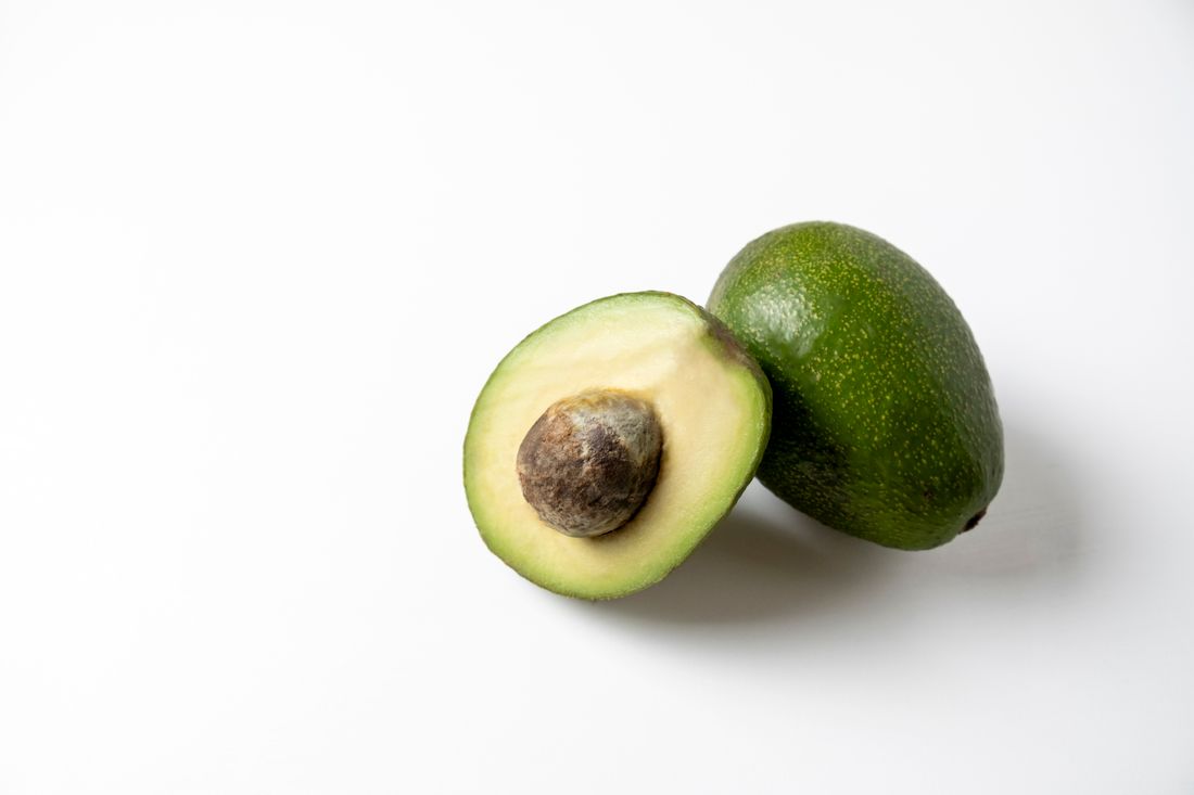 A whole avocado beside a cut avocado half